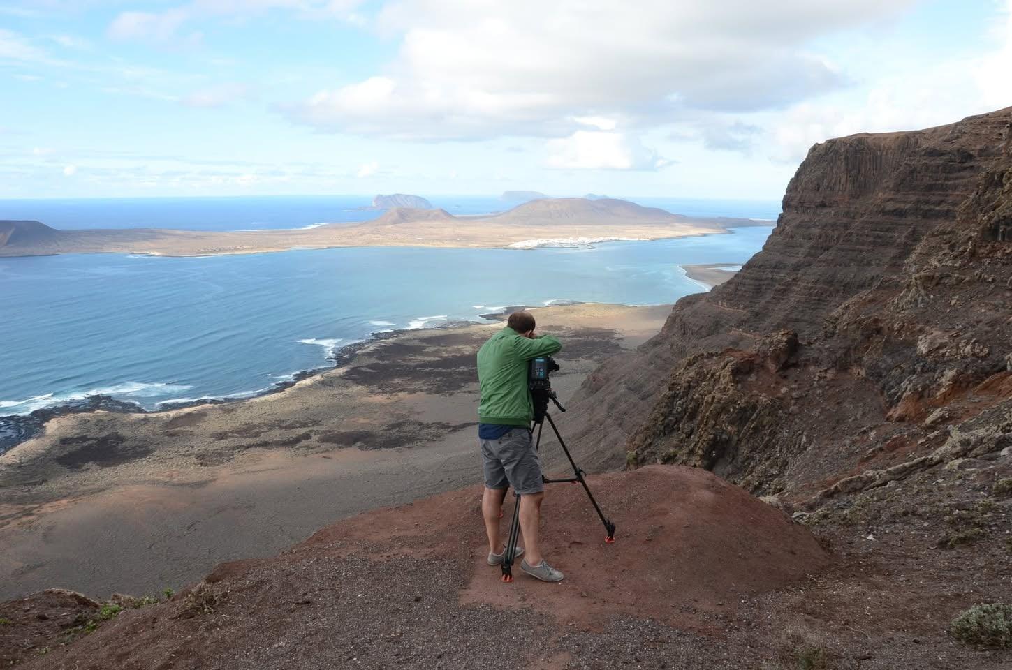 Kameramann mit Stativ auf einer Klippe über dem Meer